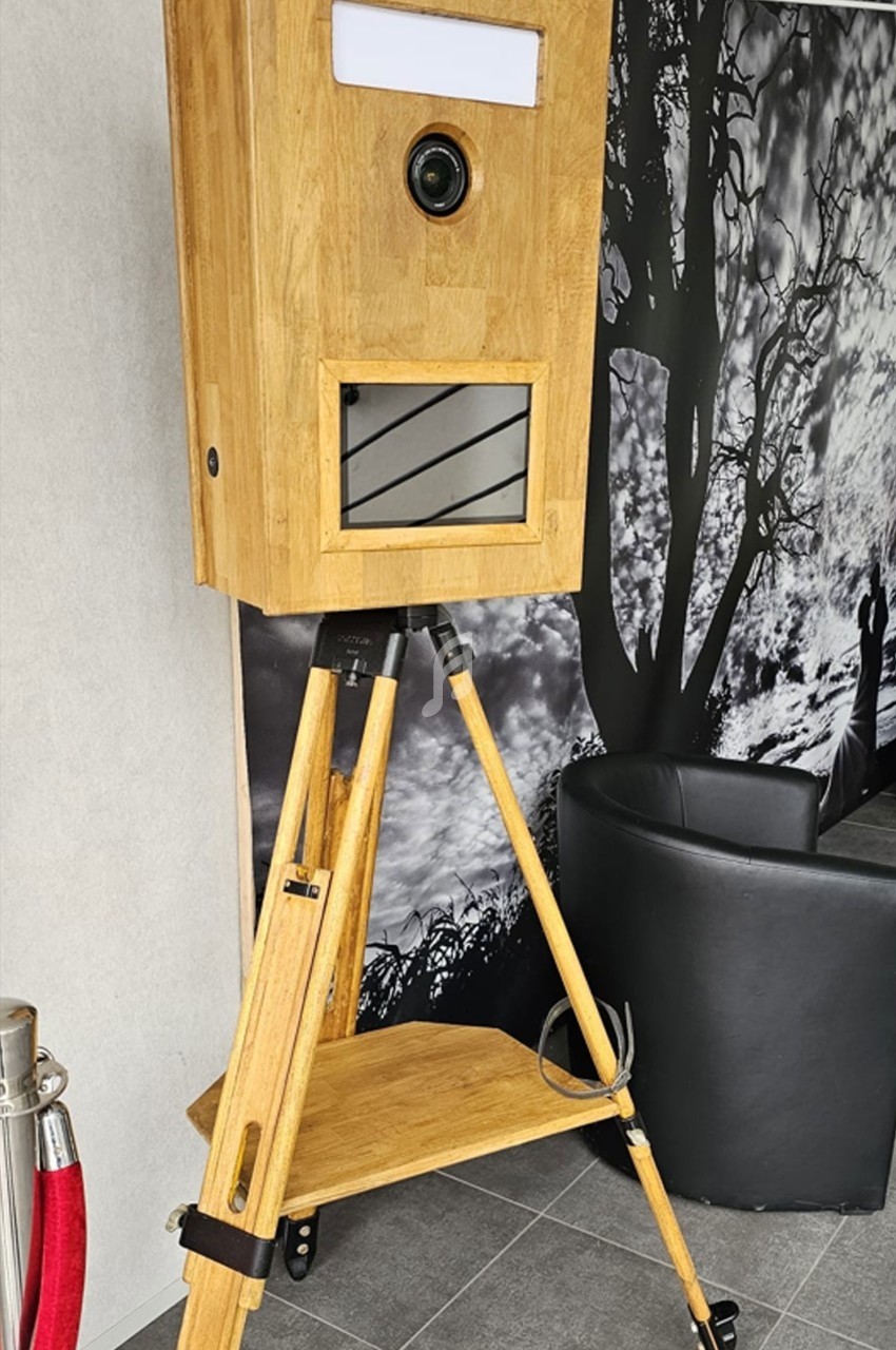 Borne photo en bois sur trépied, équipée d'un objectif et d'un écran, installée dans un espace intérieur moderne.