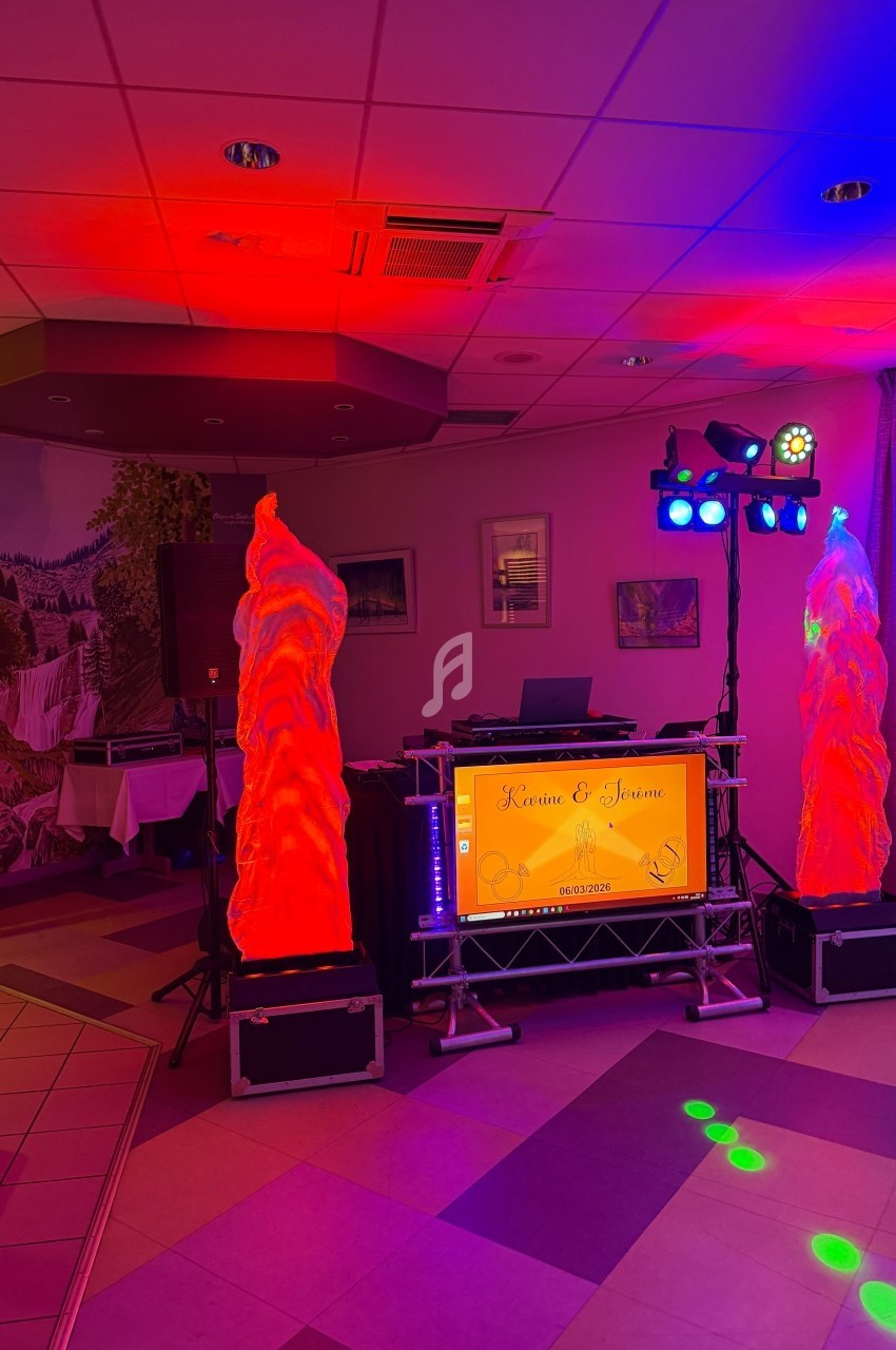 Installation de DJ avec éclairage coloré et écran personnalisé dans une salle décorée pour un événement.