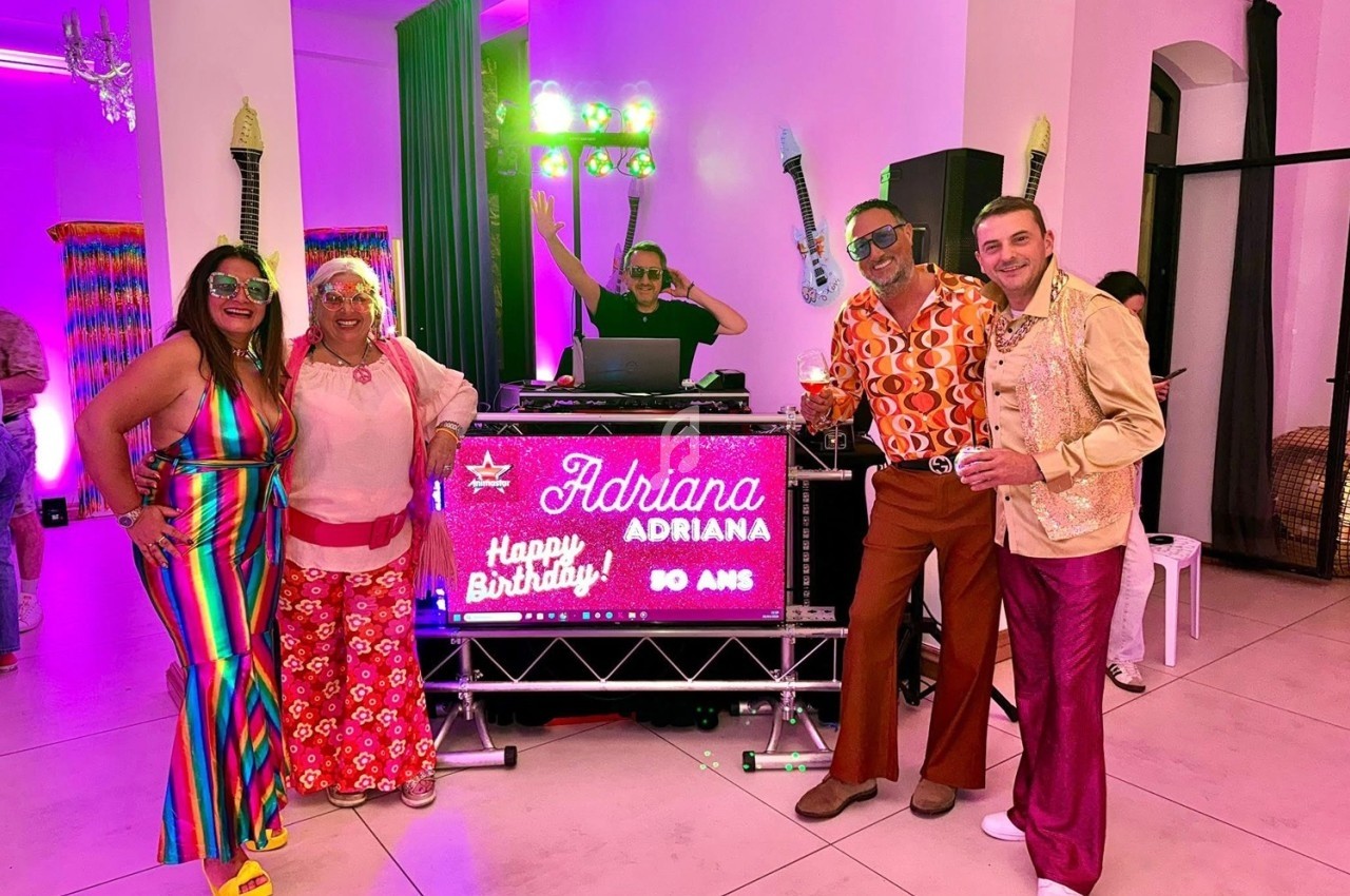 Des personnes en tenues colorées posent devant un DJ et une décoration lumineuse pour une fête d'anniversaire.