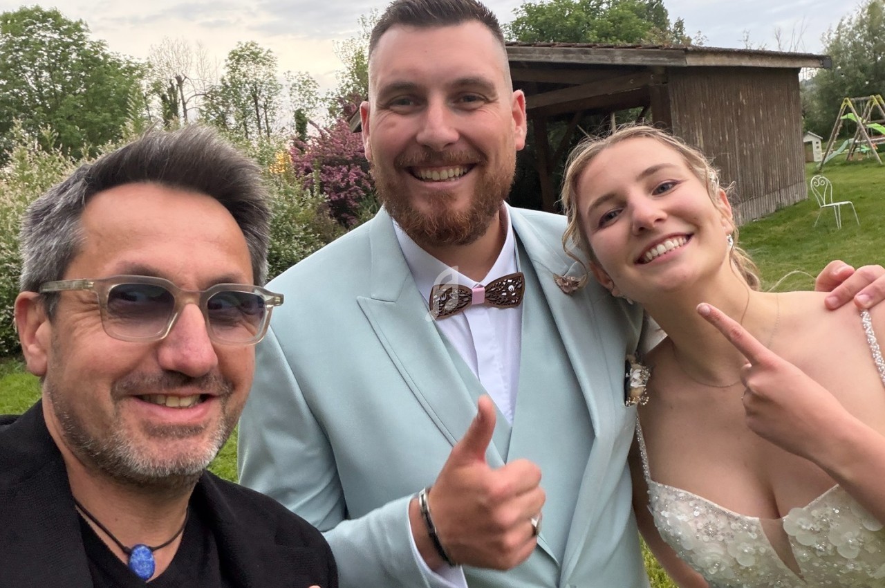 Trois personnes souriantes posent devant un jardin avec un bâtiment en bois en arrière-plan.