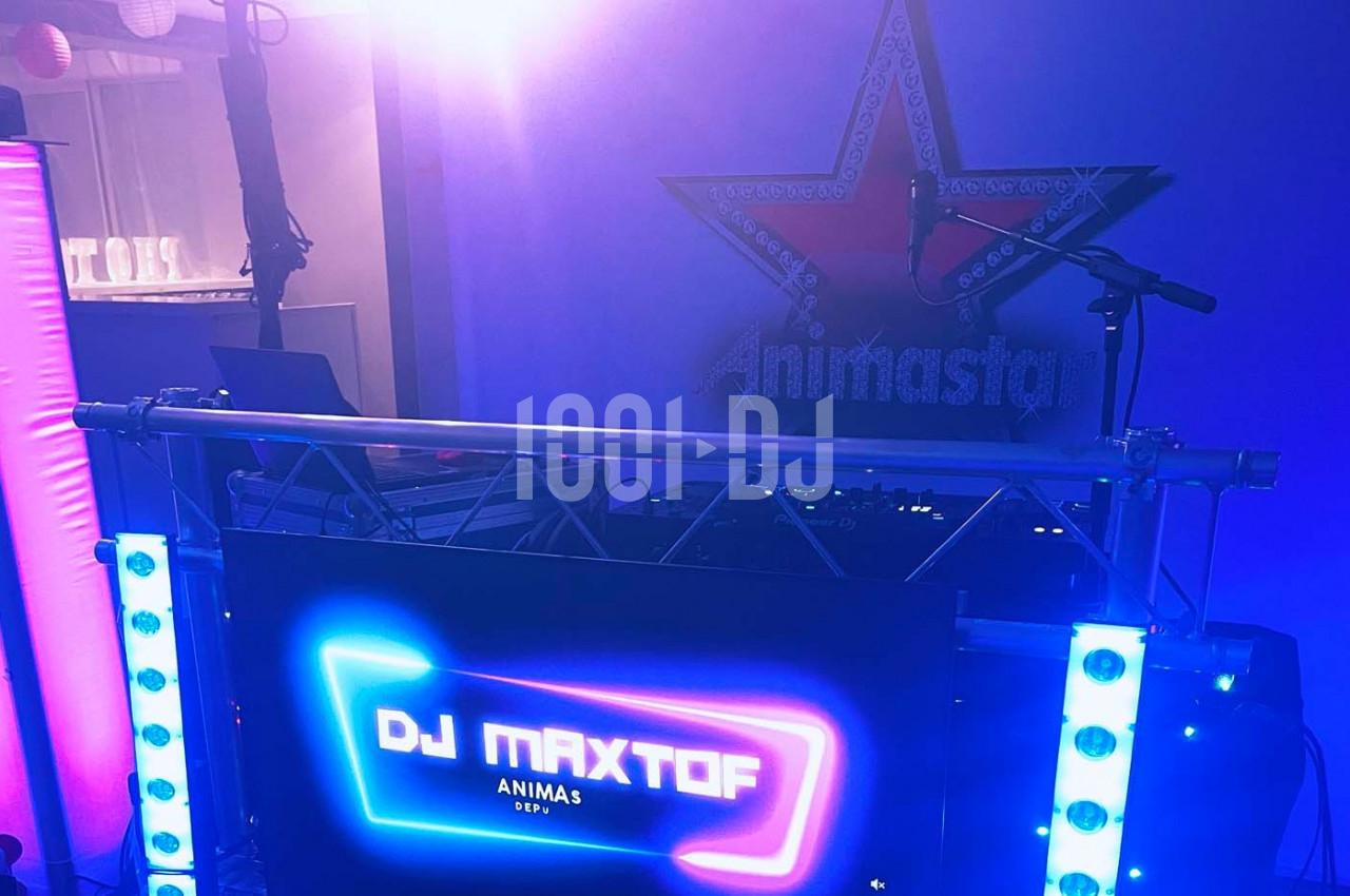 Poste de DJ avec écran lumineux affichant ’DJ MAXTOF’, éclairages colorés et décor en arrière-plan.