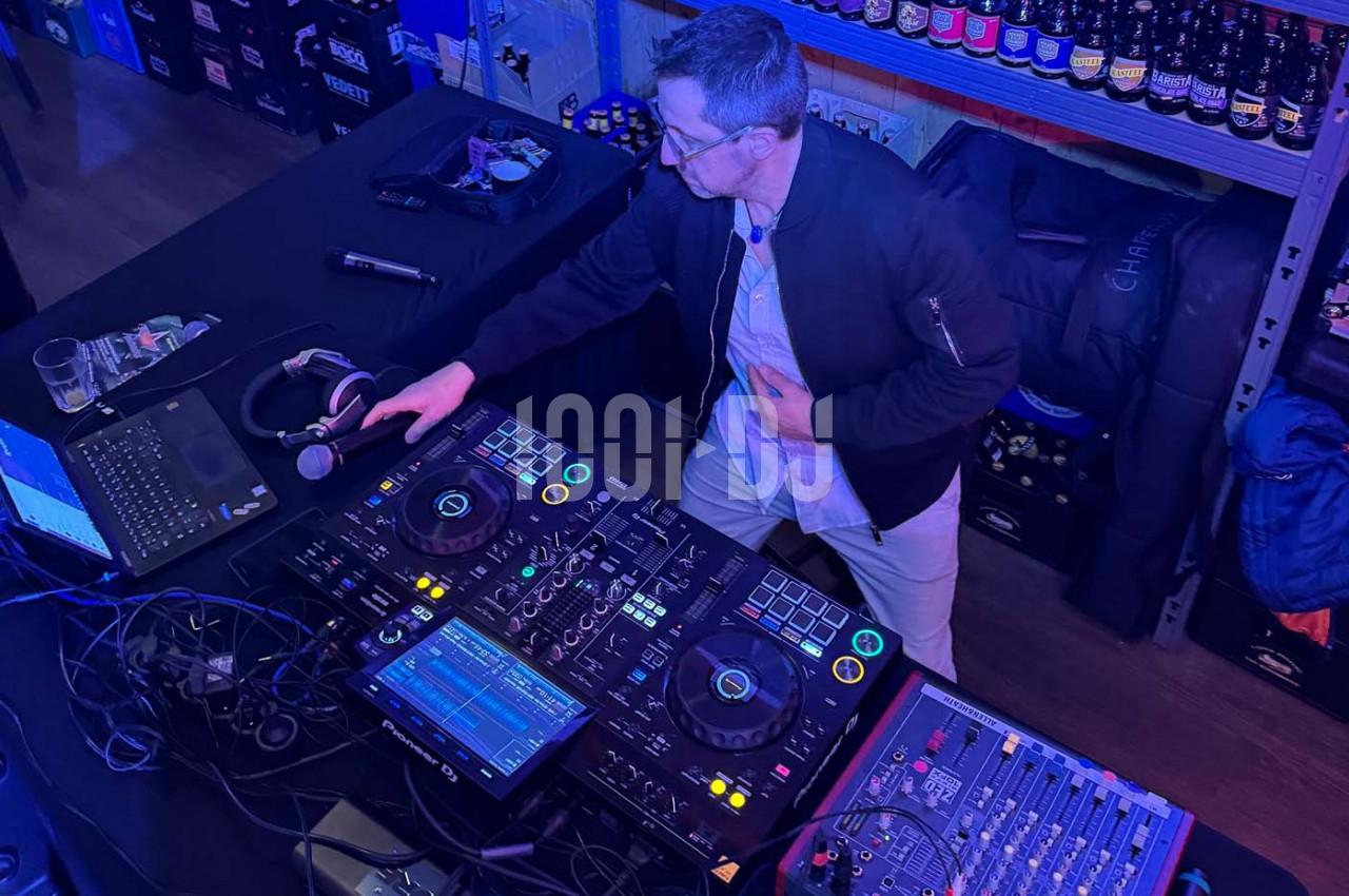 Un DJ mixe de la musique sur une console dans un environnement éclairé par des lumières bleues, entouré d'équipements.