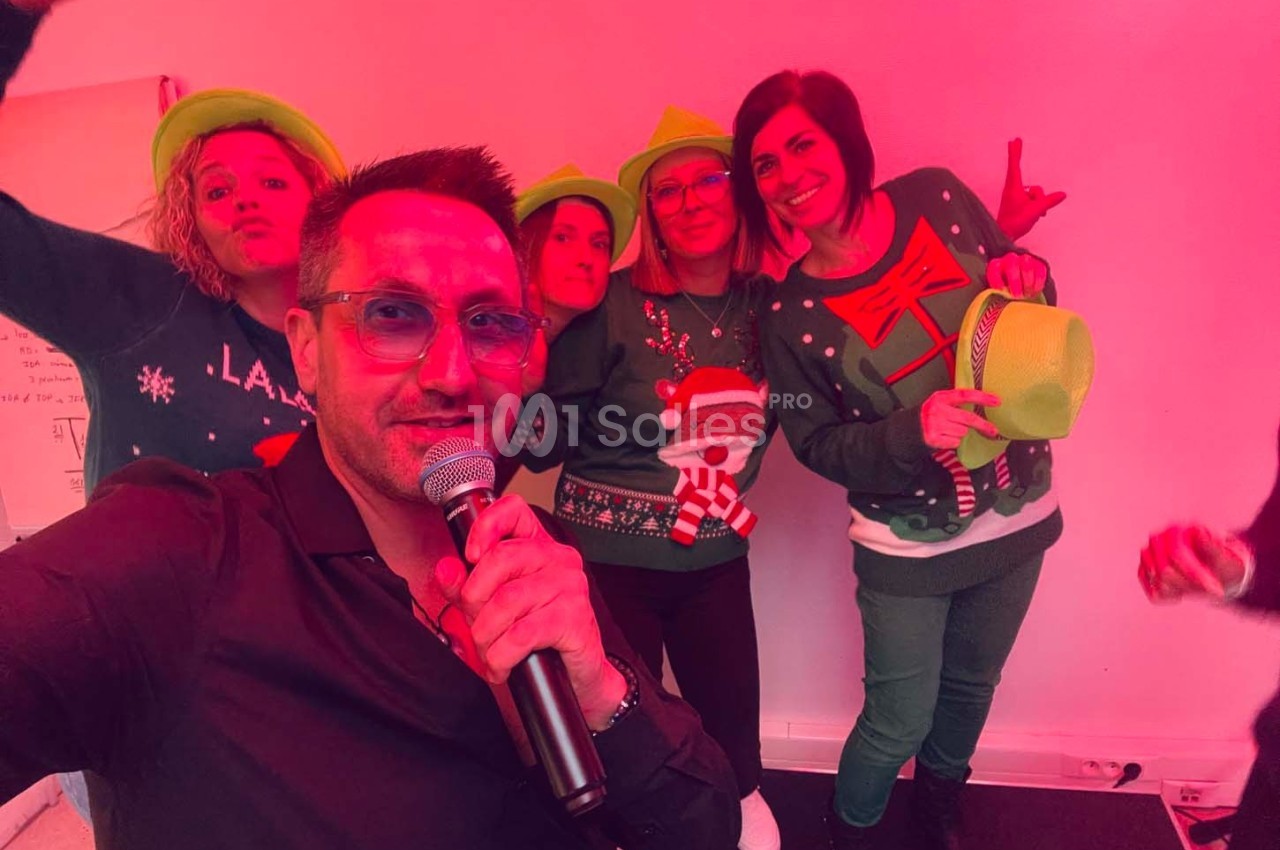 Un groupe de personnes en tenues festives pose dans une ambiance lumineuse rouge, l'une tenant un micro.