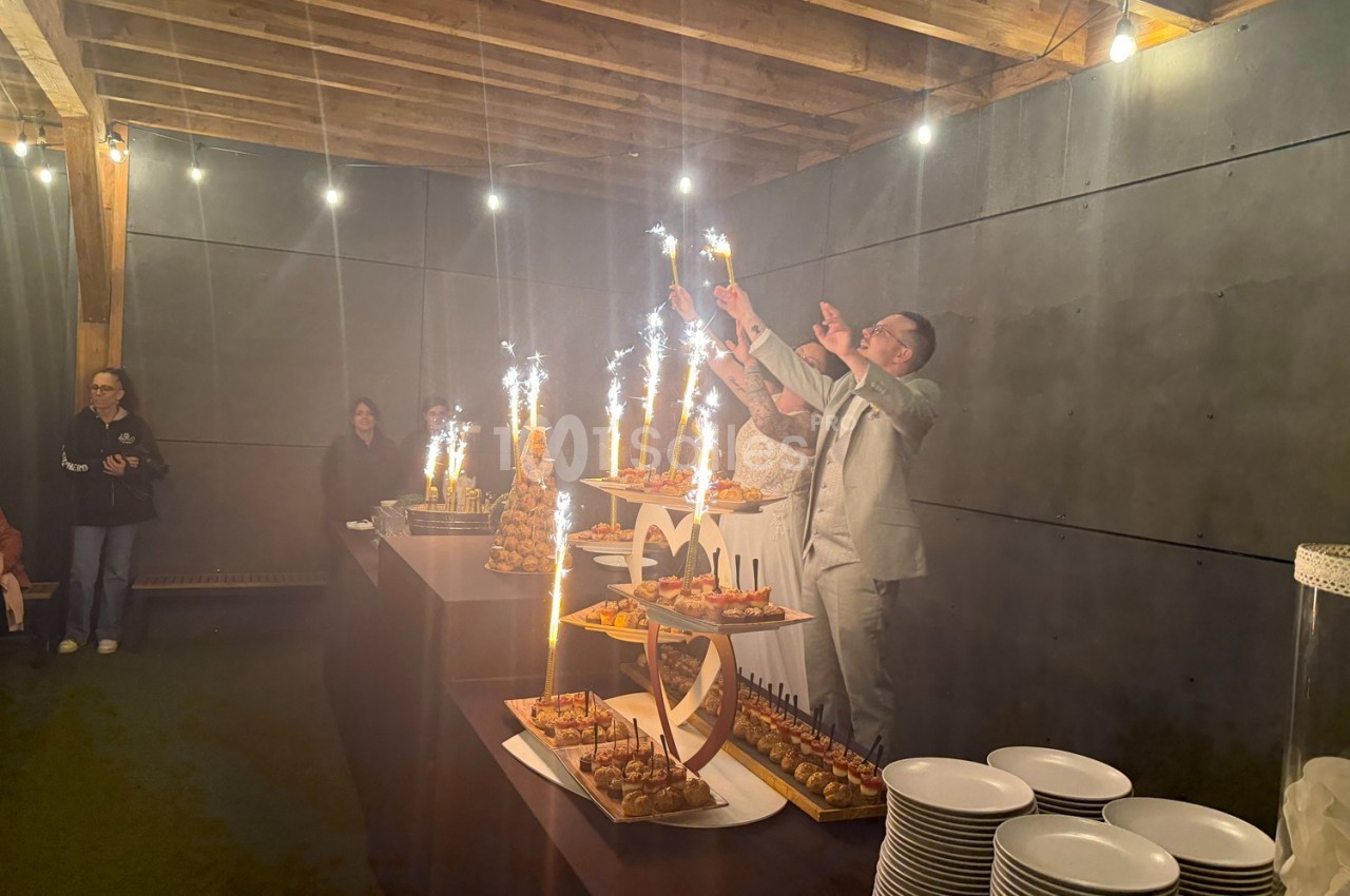 Des personnes célèbrent avec des coupes et des fontaines lumineuses autour d'un buffet dans une salle éclairée.