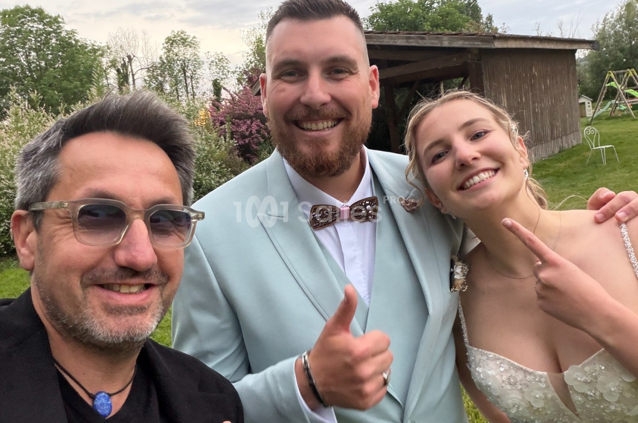 Trois personnes souriantes posent devant un jardin avec un bâtiment en bois en arrière-plan.