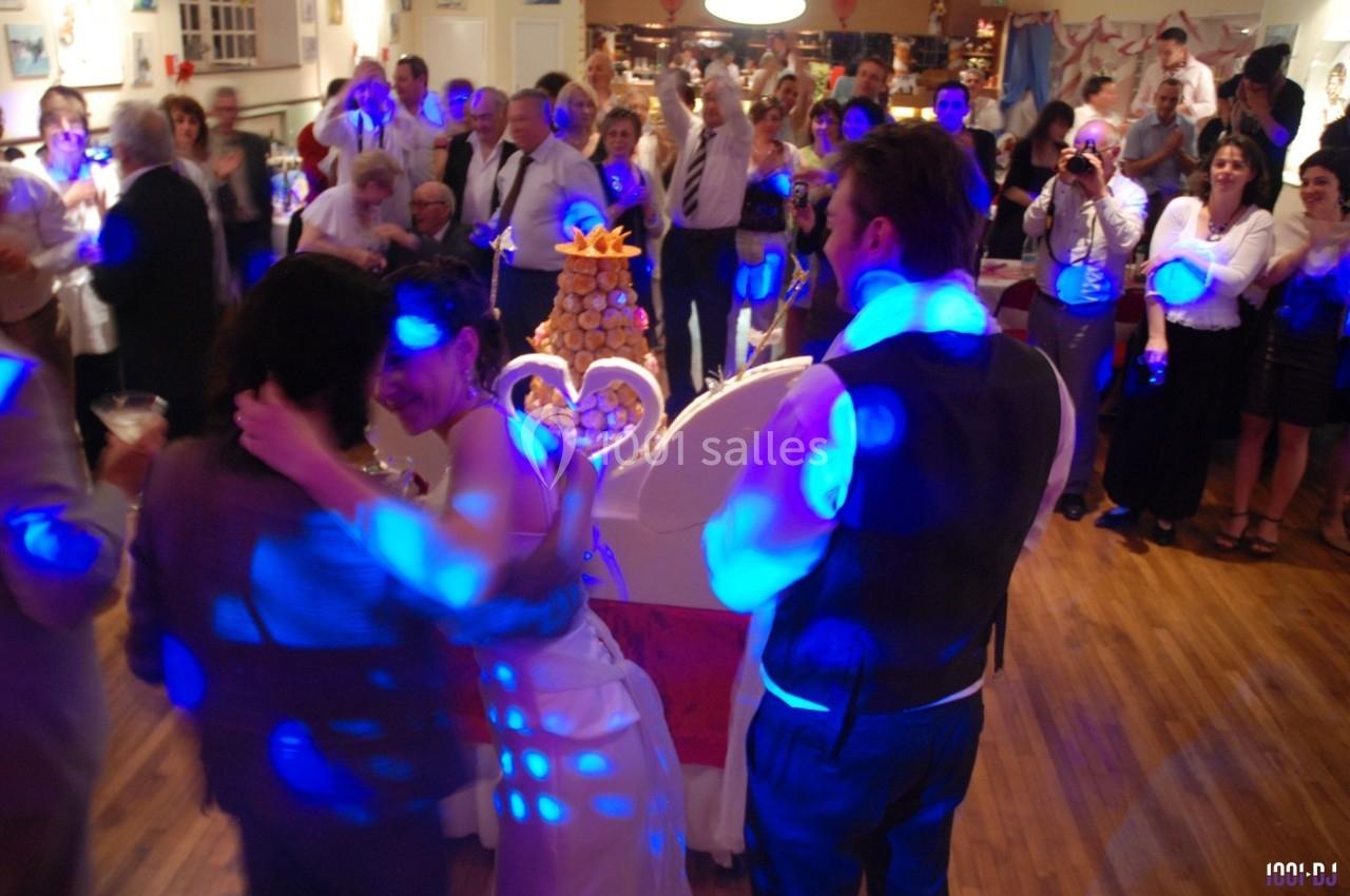 Des invités dansent et célèbrent autour d'une pièce montée lors d'une réception festive dans une salle éclairée.