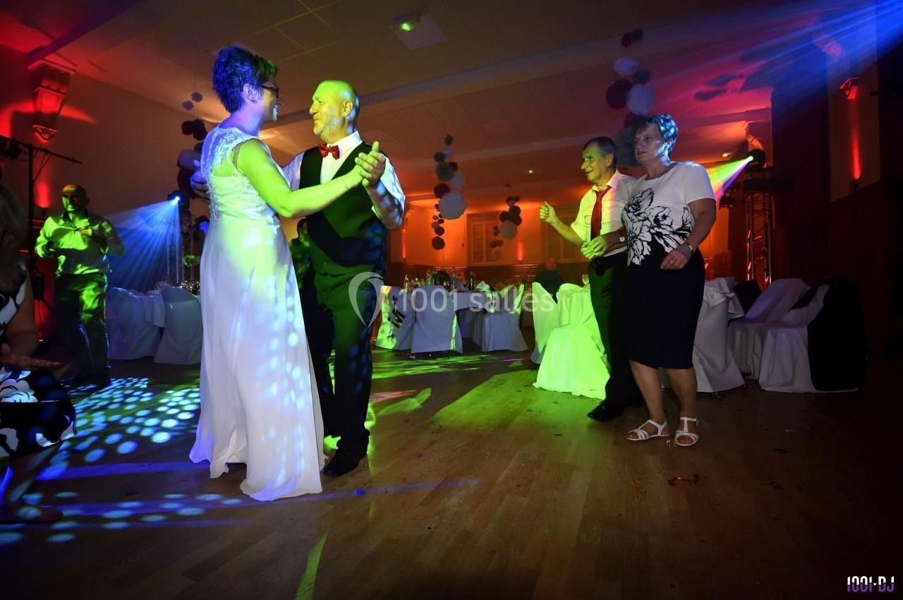 Des couples dansent sur une piste éclairée par des lumières colorées lors d'une soirée festive.