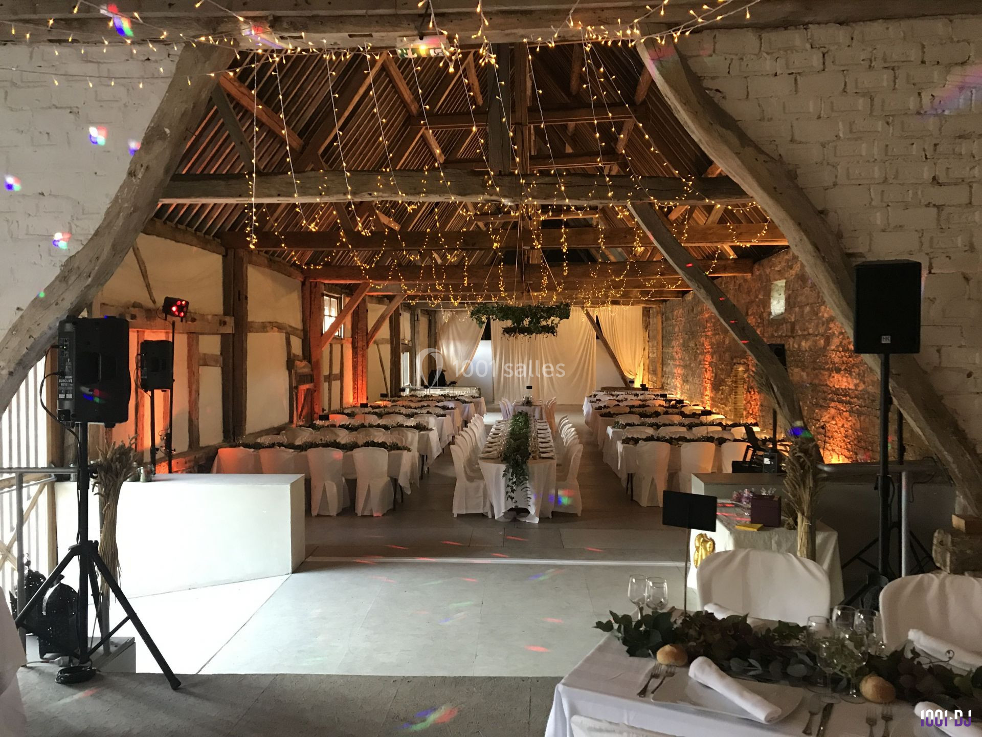 Salle de réception décorée avec des guirlandes lumineuses, des tables dressées et une ambiance chaleureuse dans une grange…
