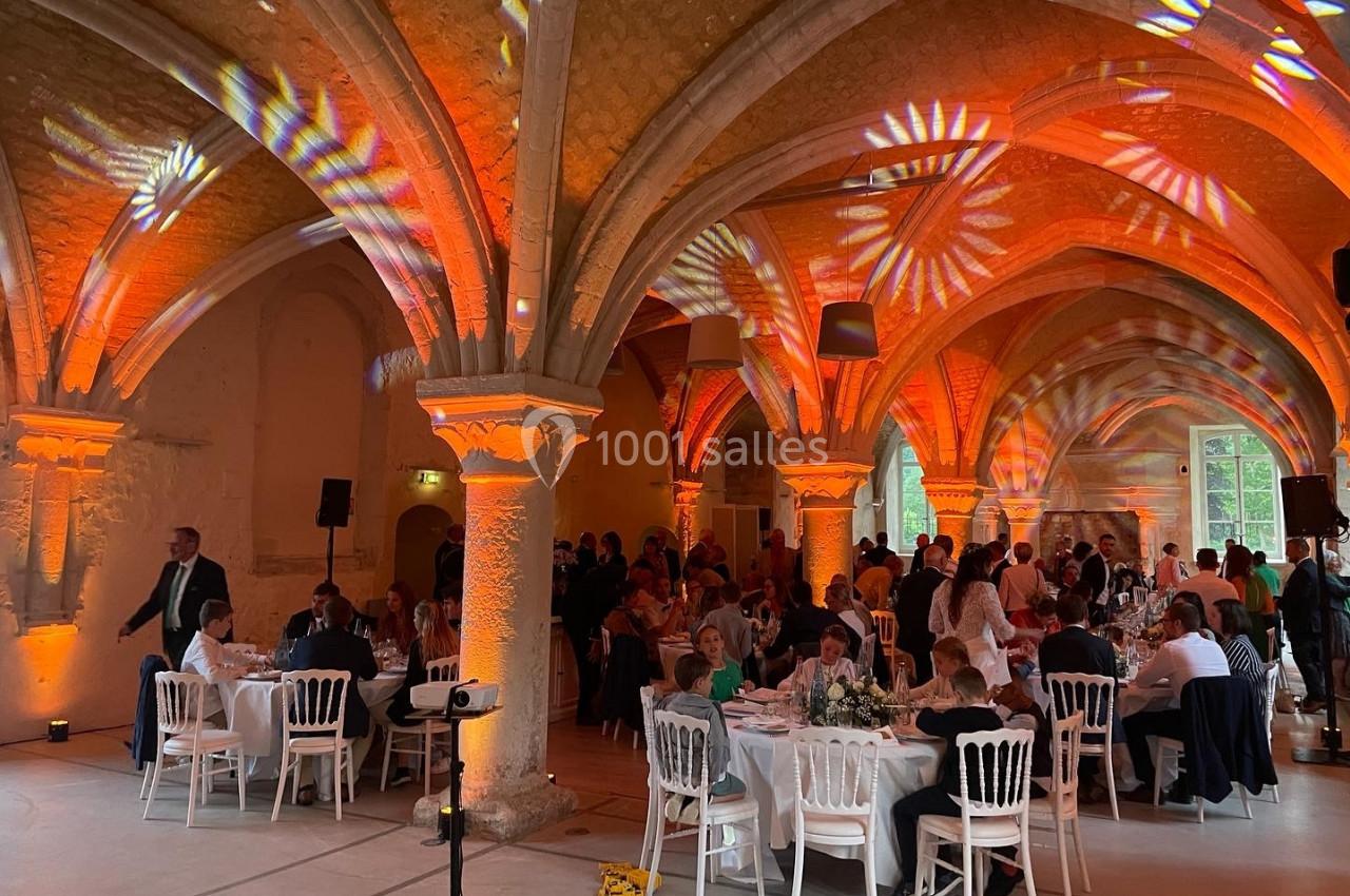 Salle voûtée éclairée de lumières orange, accueillant des convives assis à des tables rondes lors d'un événement.