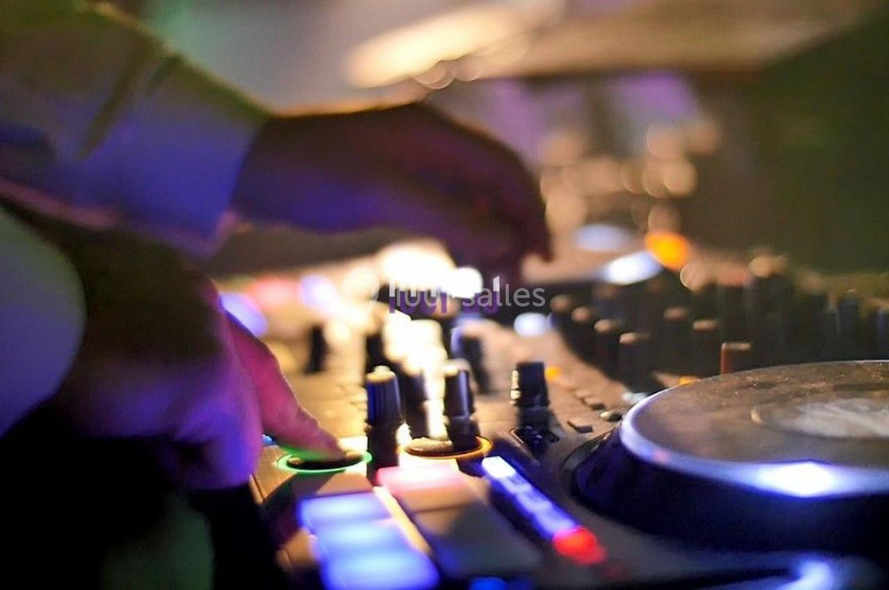 Mains ajustant des commandes sur une table de mixage lumineuse dans une ambiance tamisée.