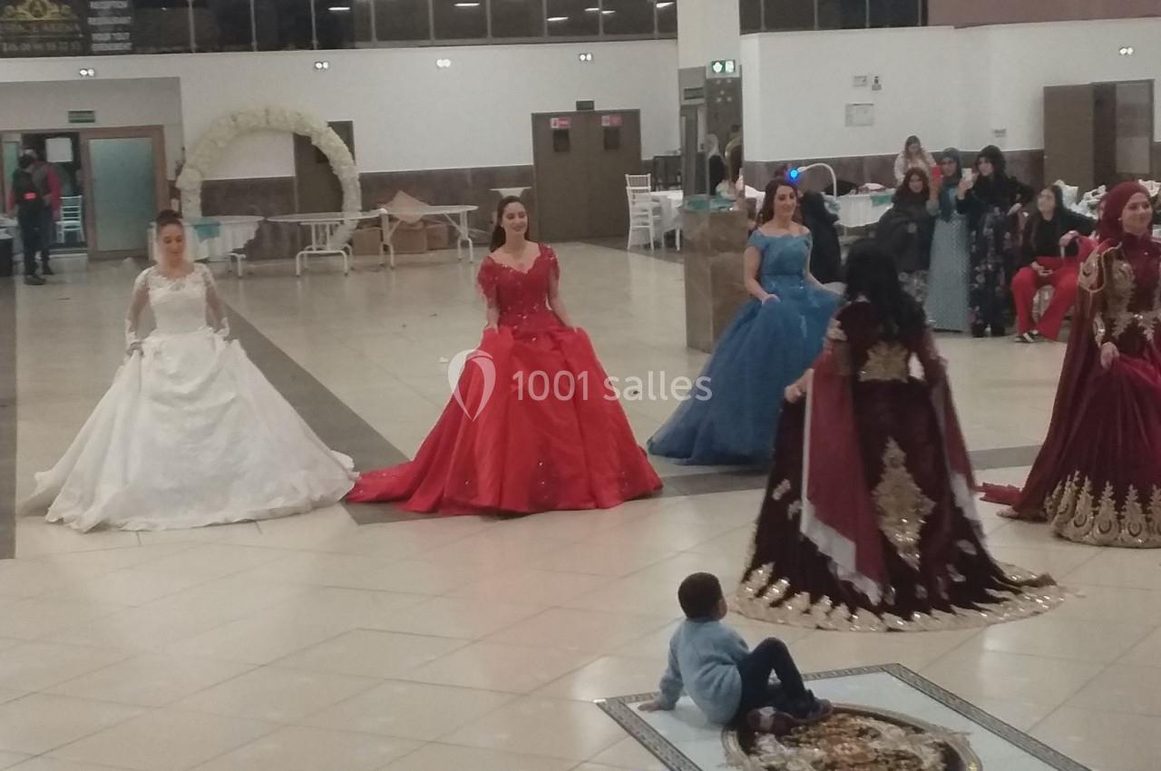 Des femmes en robes de soirée colorées dans une salle de réception, entourées de quelques invités et d'enfants.
