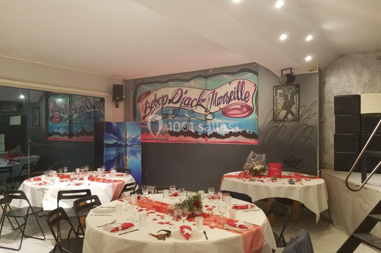 Salle décorée pour un événement avec des tables dressées, des nappes blanches et une fresque murale ’Bébé Rock Marseille’.