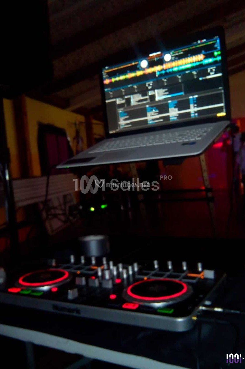 Console de mixage DJ avec un ordinateur portable affichant un logiciel de musique, dans un environnement sombre.