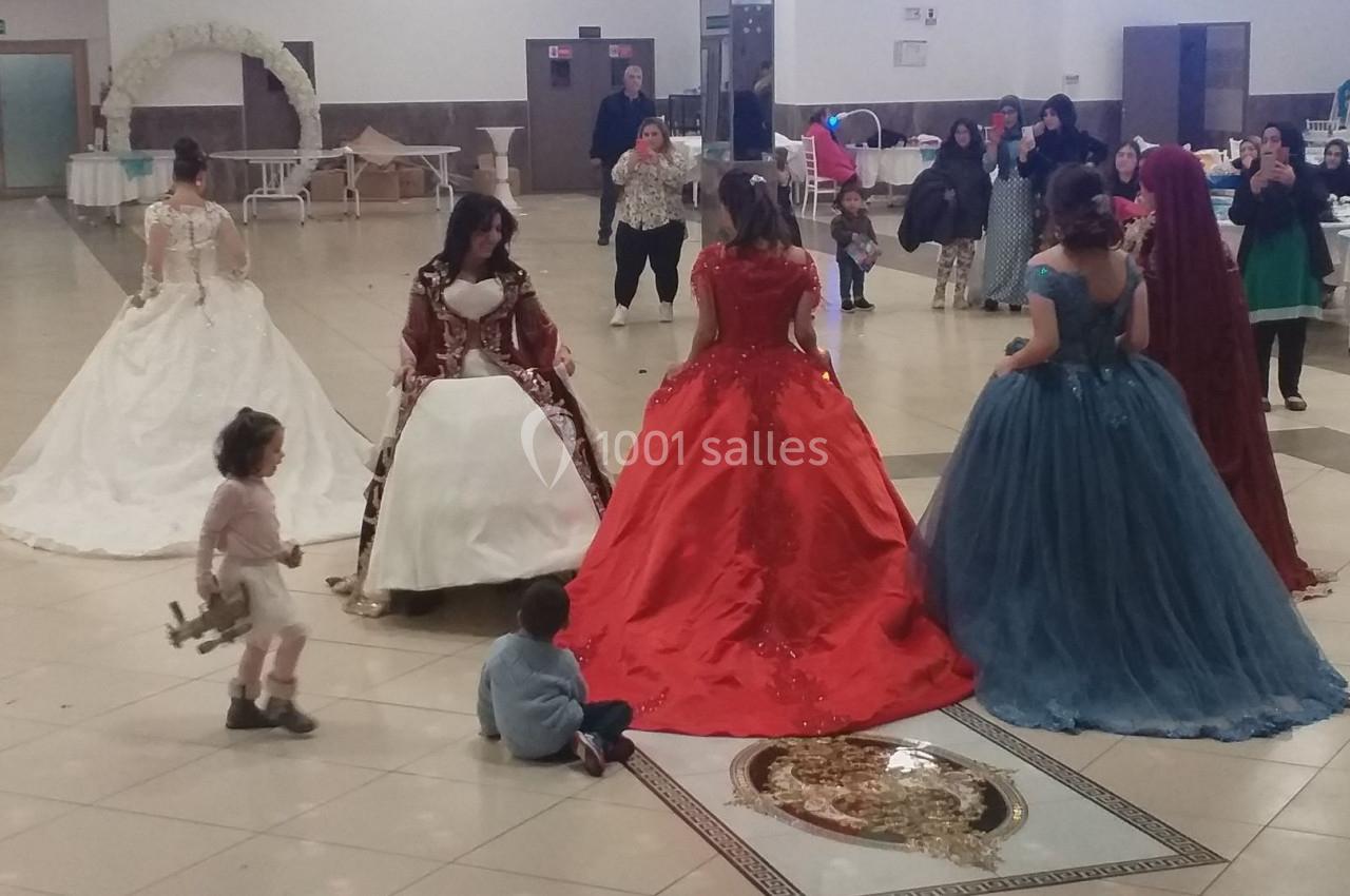 Des femmes en robes de soirée colorées discutent dans une grande salle avec des enfants assis au sol.