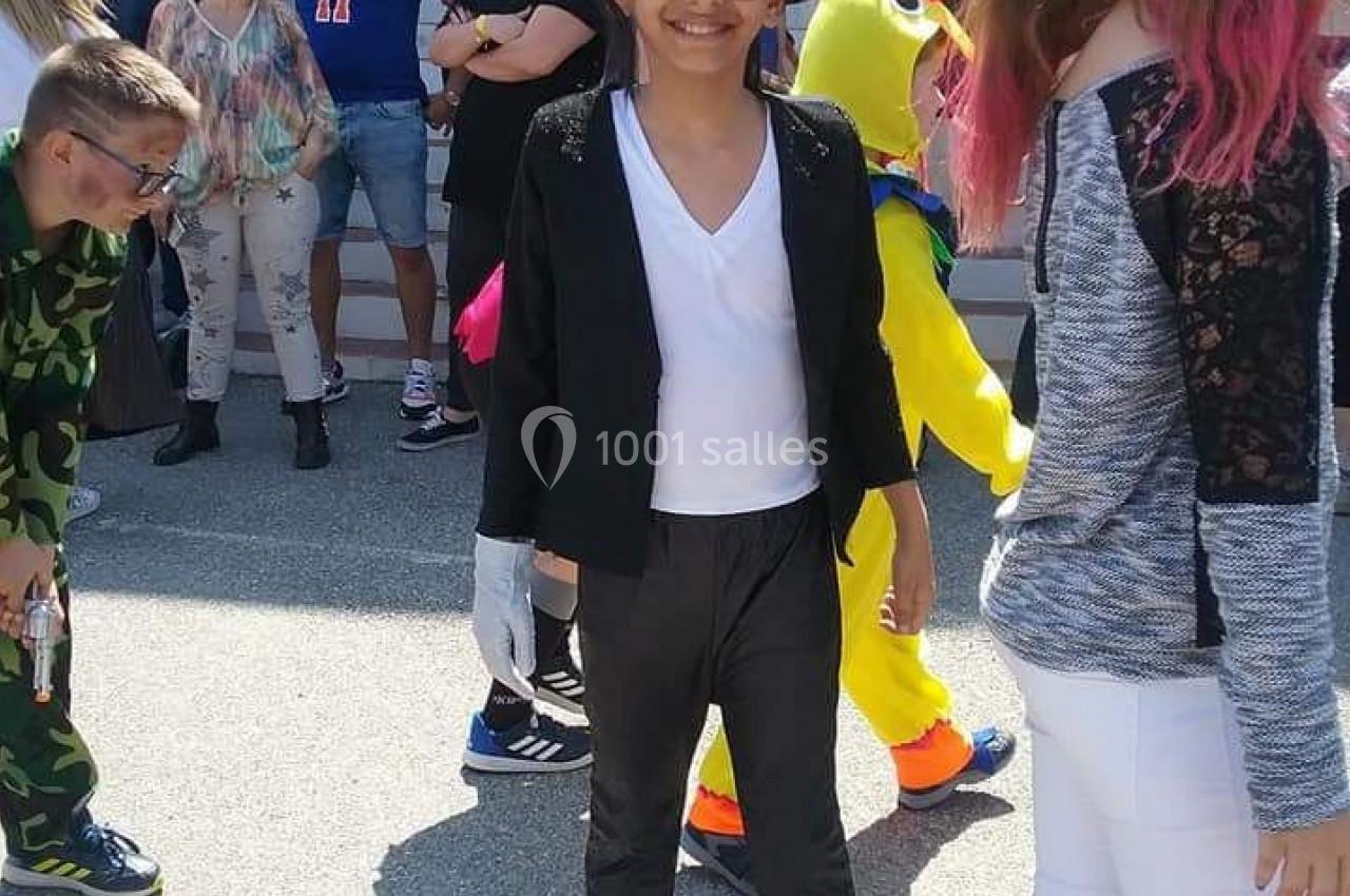 Un enfant déguisé en tenue noire et blanche sourit au milieu d'une foule lors d'un événement en extérieur.