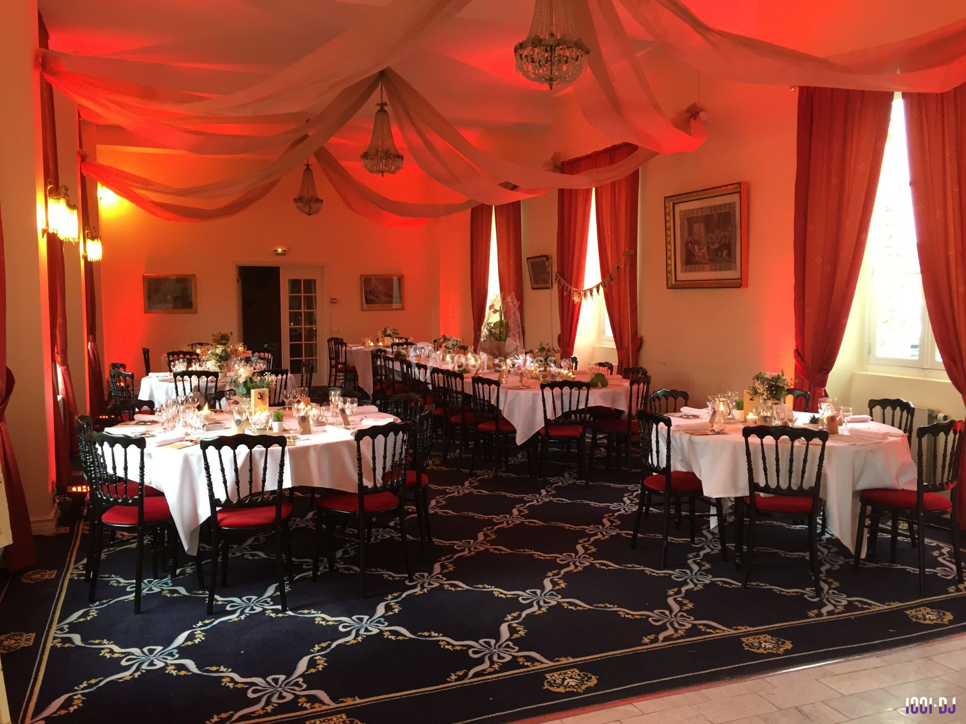 Salle de réception décorée avec des tables dressées, des chaises noires et rouges, et un éclairage rouge chaleureux.