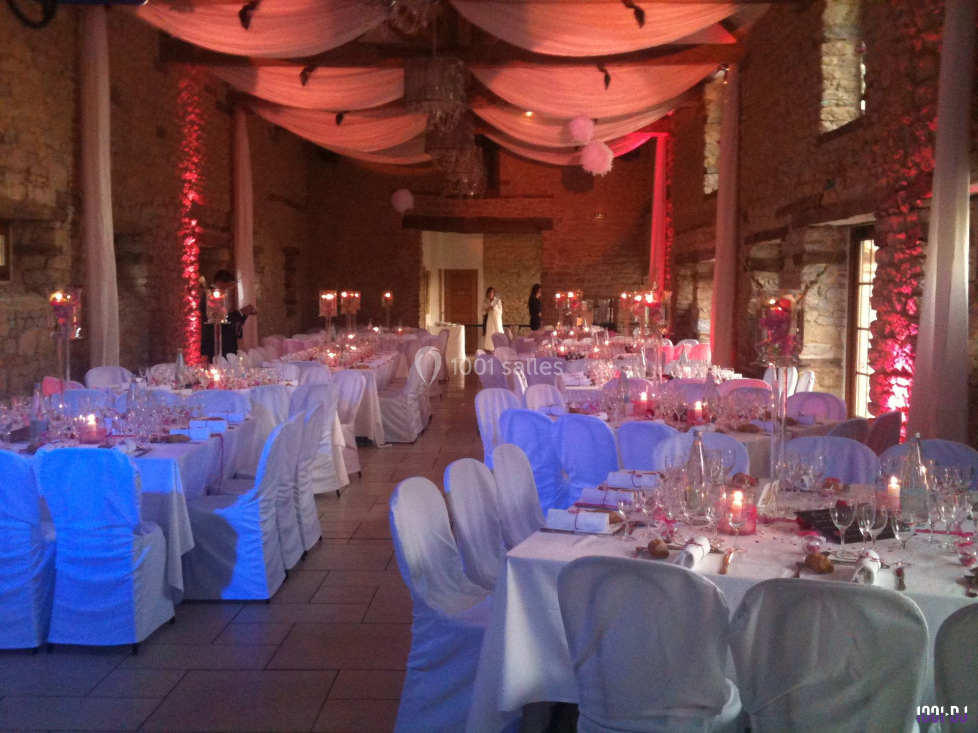 Salle de réception décorée pour un mariage, avec tables dressées, chaises blanches et éclairage tamisé.
