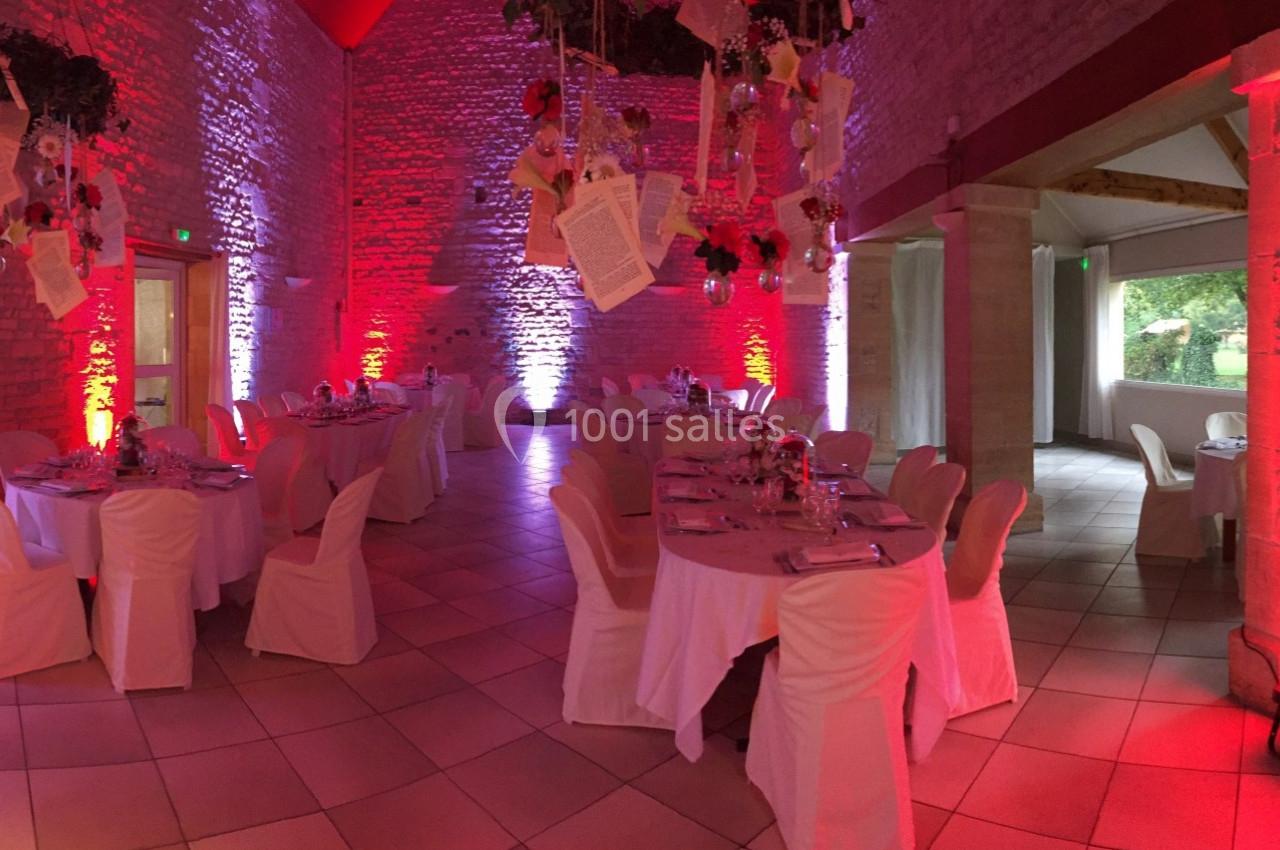 Salle en pierres apparentes décorée pour un événement, avec tables dressées et éclairage rouge et blanc.