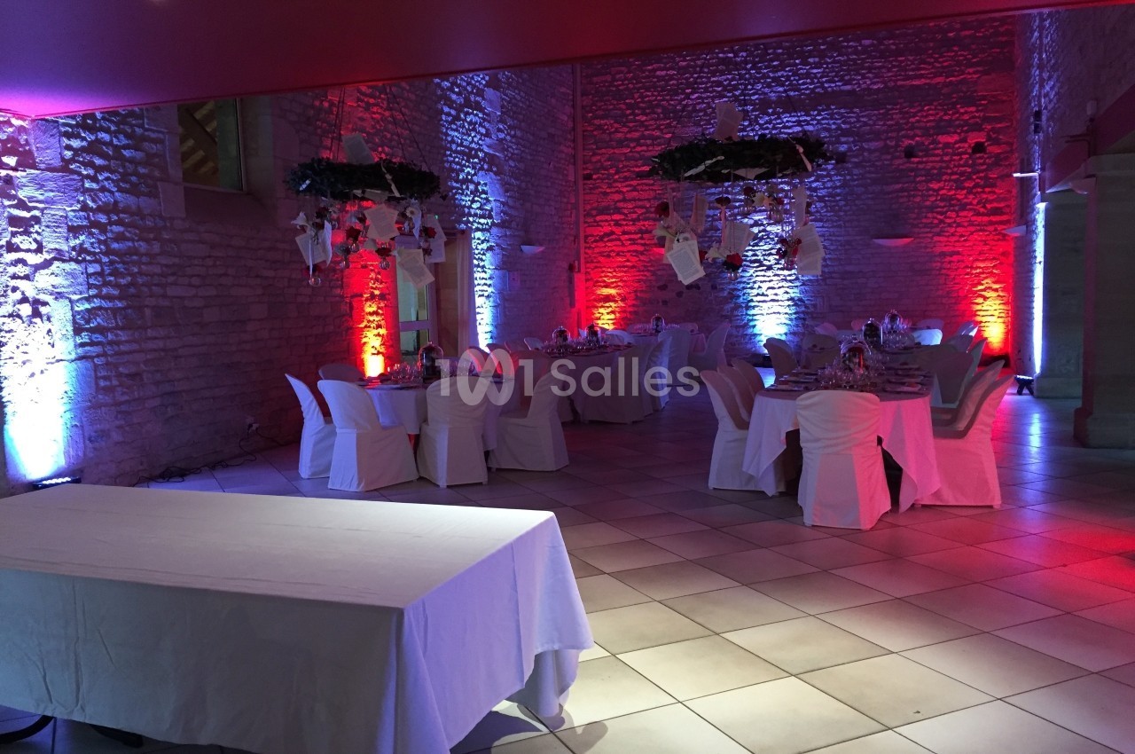 Salle de réception en pierre éclairée de lumières colorées, avec tables dressées et décorations suspendues.