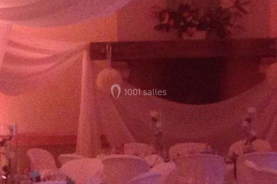 Salle de réception décorée avec des voilages blancs, des tables dressées et des chaises couvertes de housses.