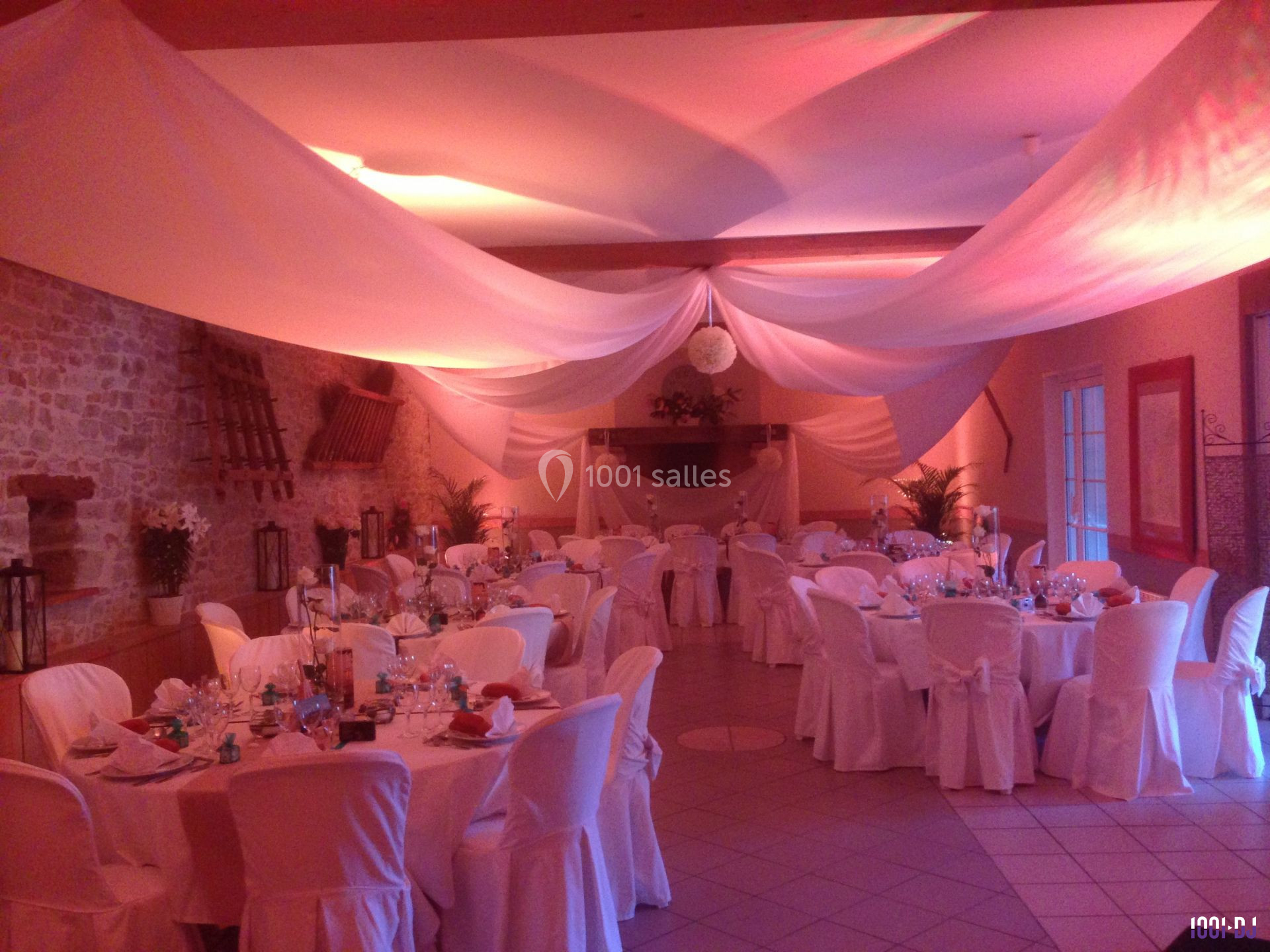 Salle de réception décorée avec des nappes blanches, des tables dressées et un éclairage tamisé.