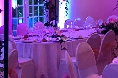 Salle de réception décorée avec des voilages blancs, des tables dressées et des chaises couvertes de housses.