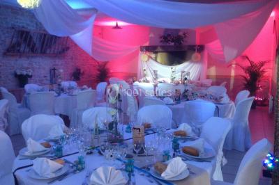 Salle de réception décorée avec des voilages blancs, des tables dressées et des chaises couvertes de housses.