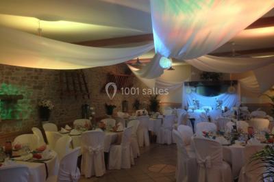 Salle de réception décorée avec des voilages blancs, des tables dressées et des chaises couvertes de housses.