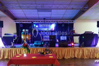 Scène éclairée avec une table de mixage, des enceintes et des affiches en arrière-plan dans une salle intérieure.