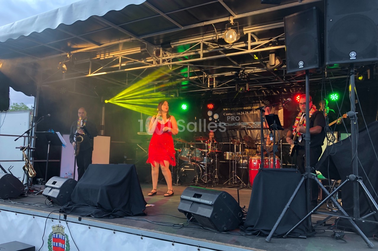 Groupe de musiciens et chanteuse en robe rouge se produisant sur une scène extérieure éclairée.