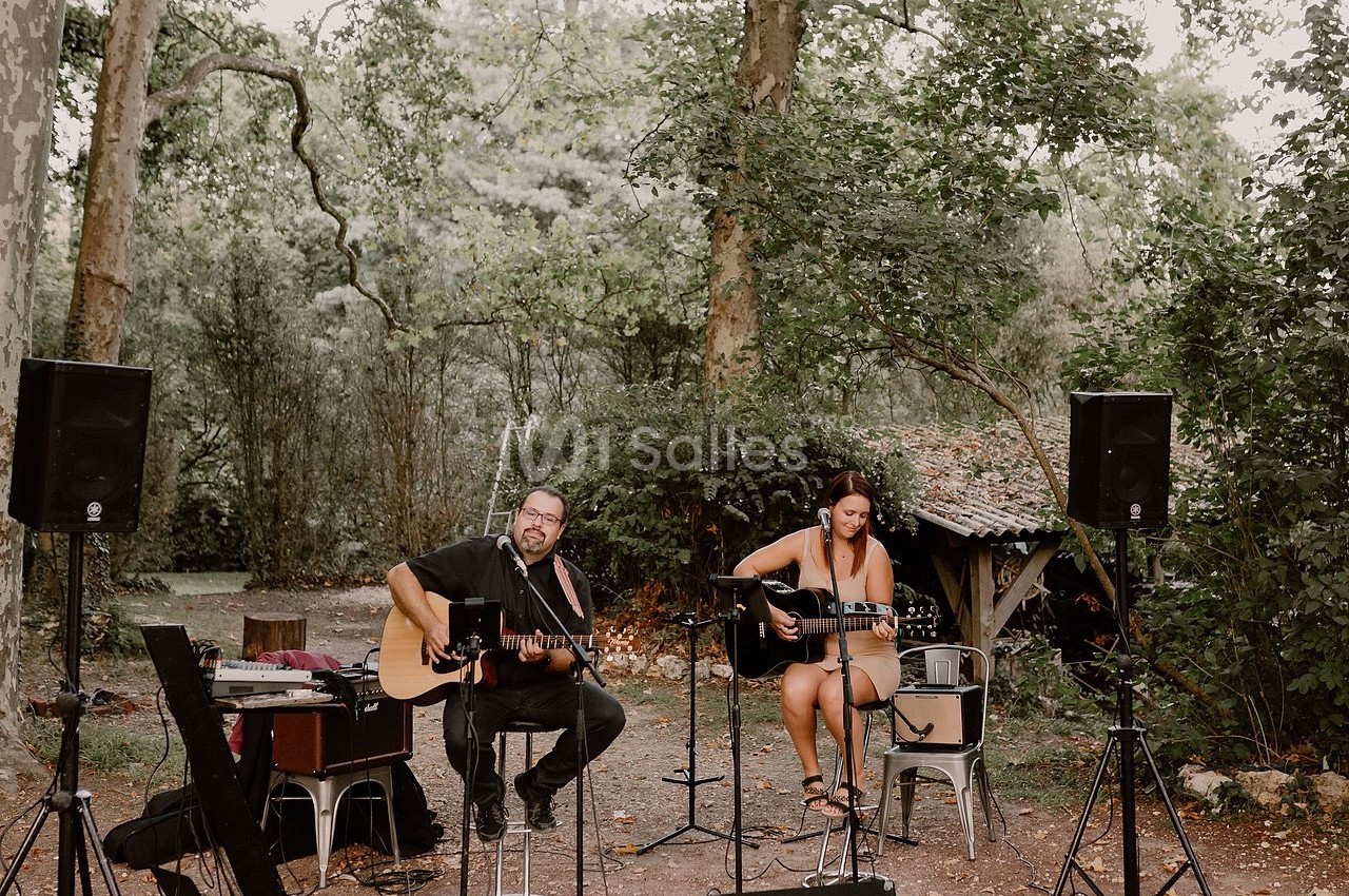 Deux musiciens jouant de la guitare acoustique en plein air, entourés d'arbres et d'équipements audio.