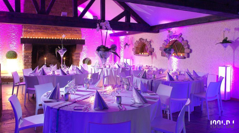 Salle de réception décorée avec des tables rondes, nappes blanches et éclairage violet créant une ambiance festive.