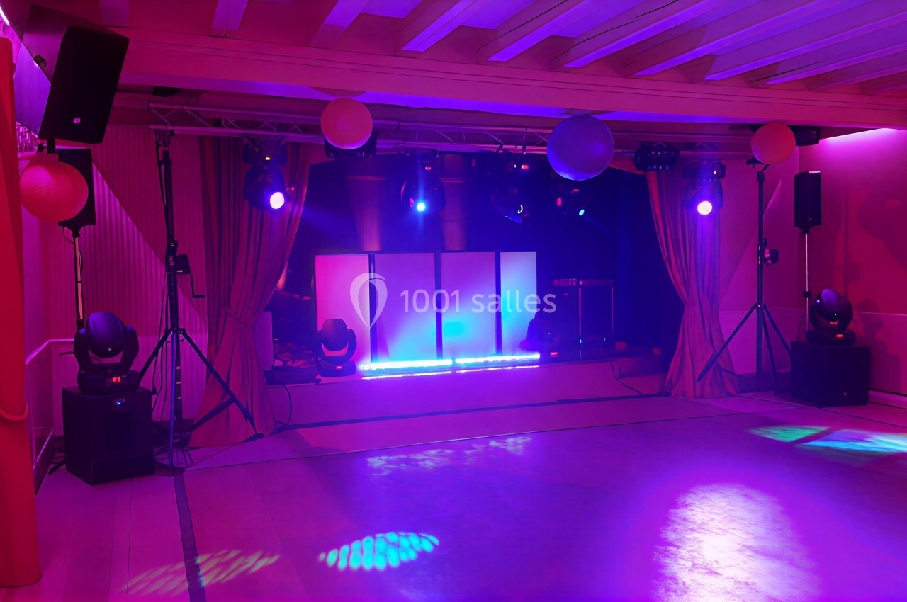 Salle de réception avec éclairage coloré, scène équipée de lumières et rideaux encadrant l'espace.