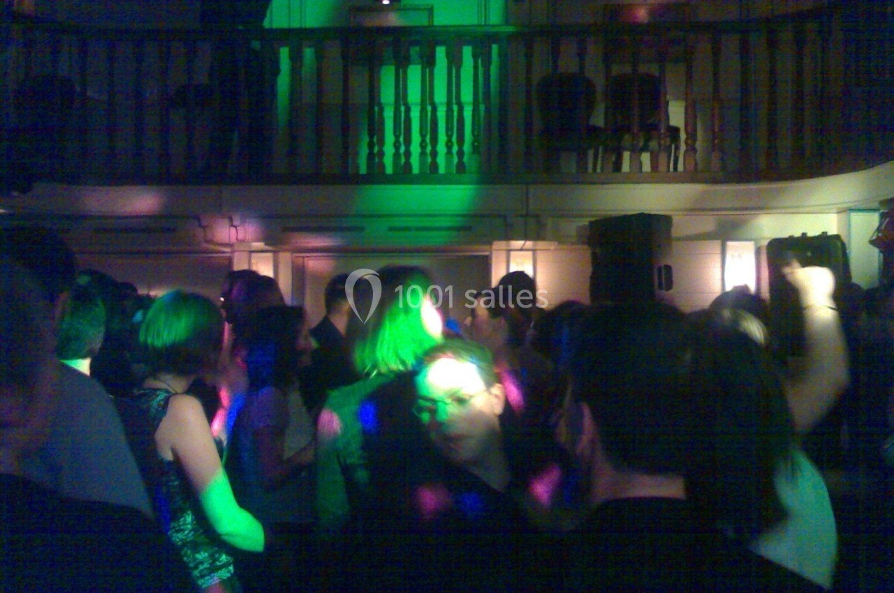 Personnes dansant dans une salle éclairée par des lumières colorées, avec une mezzanine en arrière-plan.