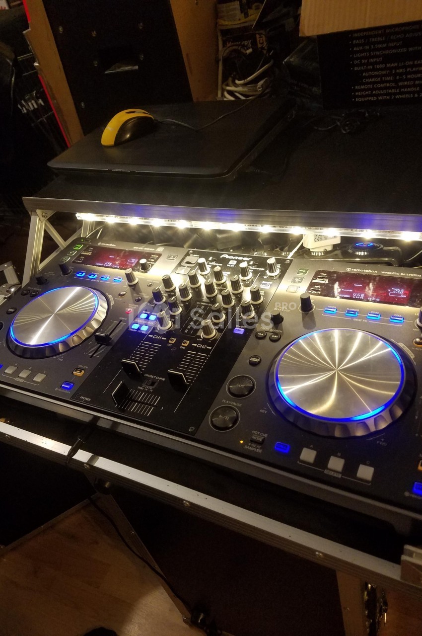 Table de mixage DJ avec platines, boutons et éclairage LED, posée sur un support dans un environnement intérieur.