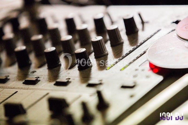 Table de mixage audio avec plusieurs boutons et potentiomètres, éclairée par une lumière tamisée.