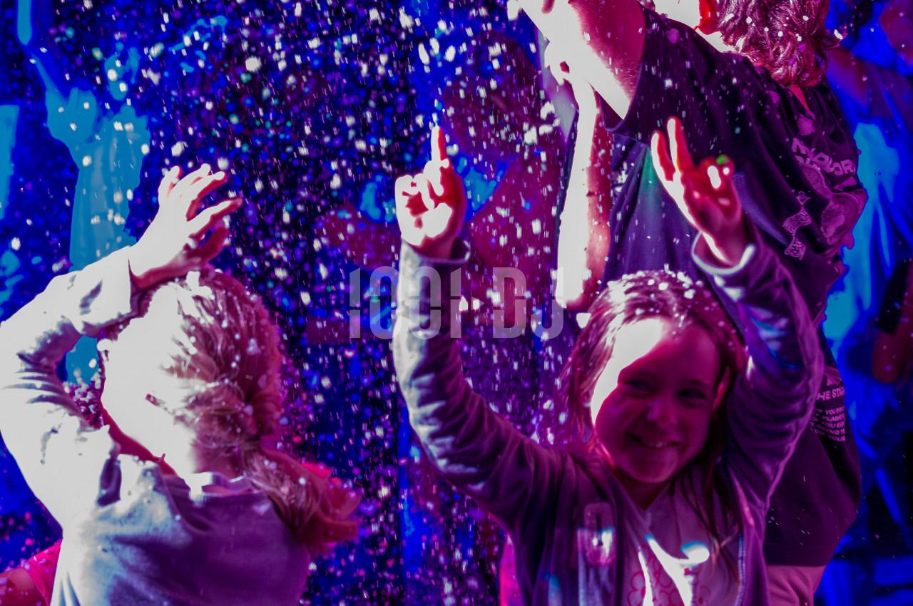 Des enfants souriants jouent sous une pluie de confettis lumineux dans une ambiance festive et colorée.