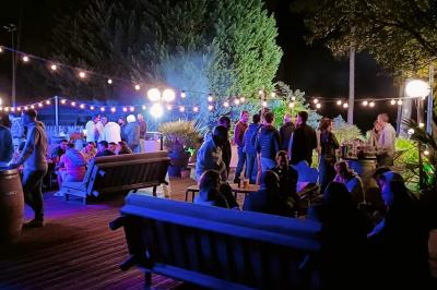 Groupe de personnes réunies en soirée en plein air, éclairées par des guirlandes lumineuses et des lampadaires.