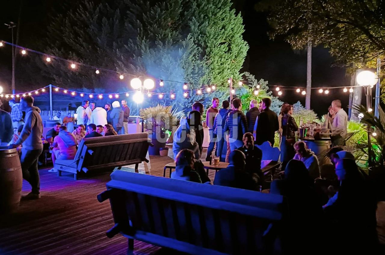 Groupe de personnes réunies en soirée en plein air, éclairées par des guirlandes lumineuses et des lampadaires.