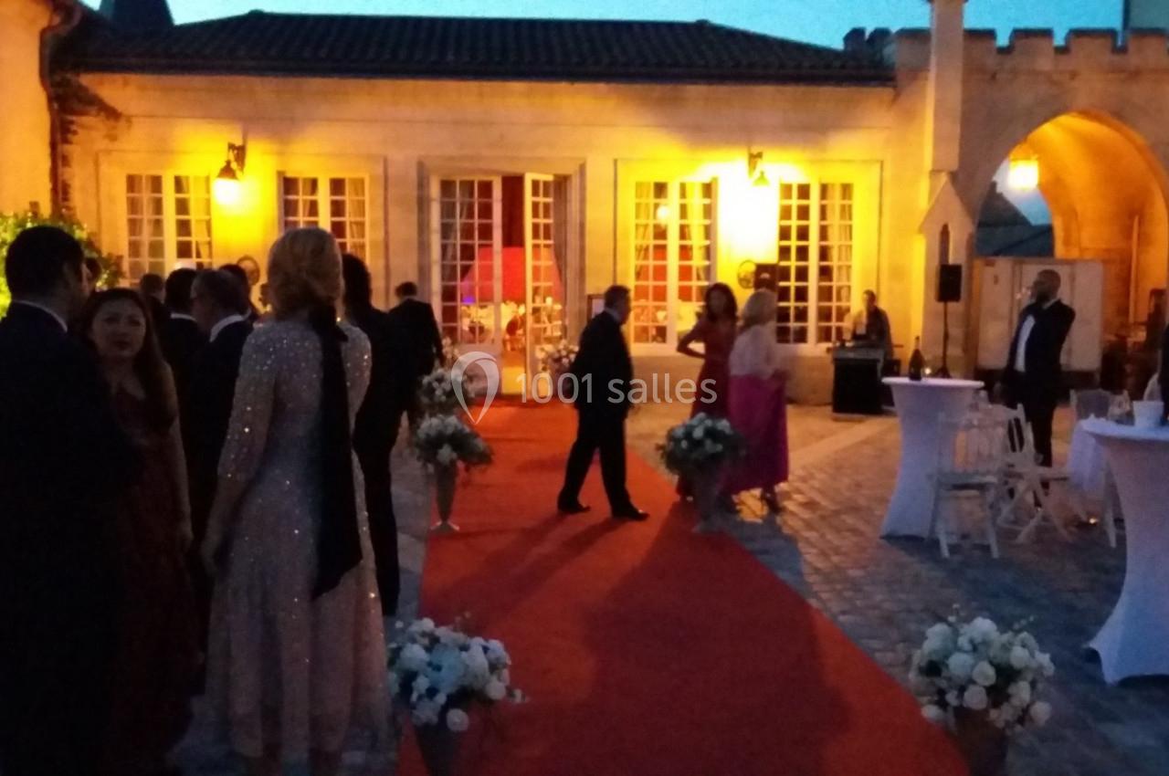 Personnes en tenue de soirée discutant sur un tapis rouge dans une cour éclairée au crépuscule.