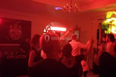 Des personnes dansent sous des lumières rouges dans une salle ornée de décorations murales et de lustres.