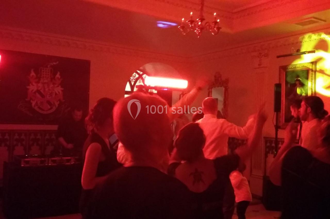 Des personnes dansent sous des lumières rouges dans une salle ornée de décorations murales et de lustres.