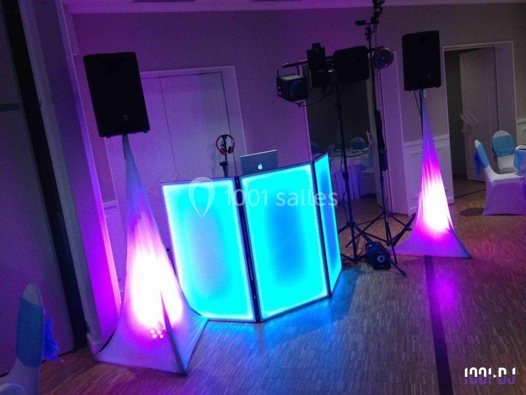 Console de DJ éclairée en bleu avec des lumières colorées et des enceintes dans une salle intérieure.