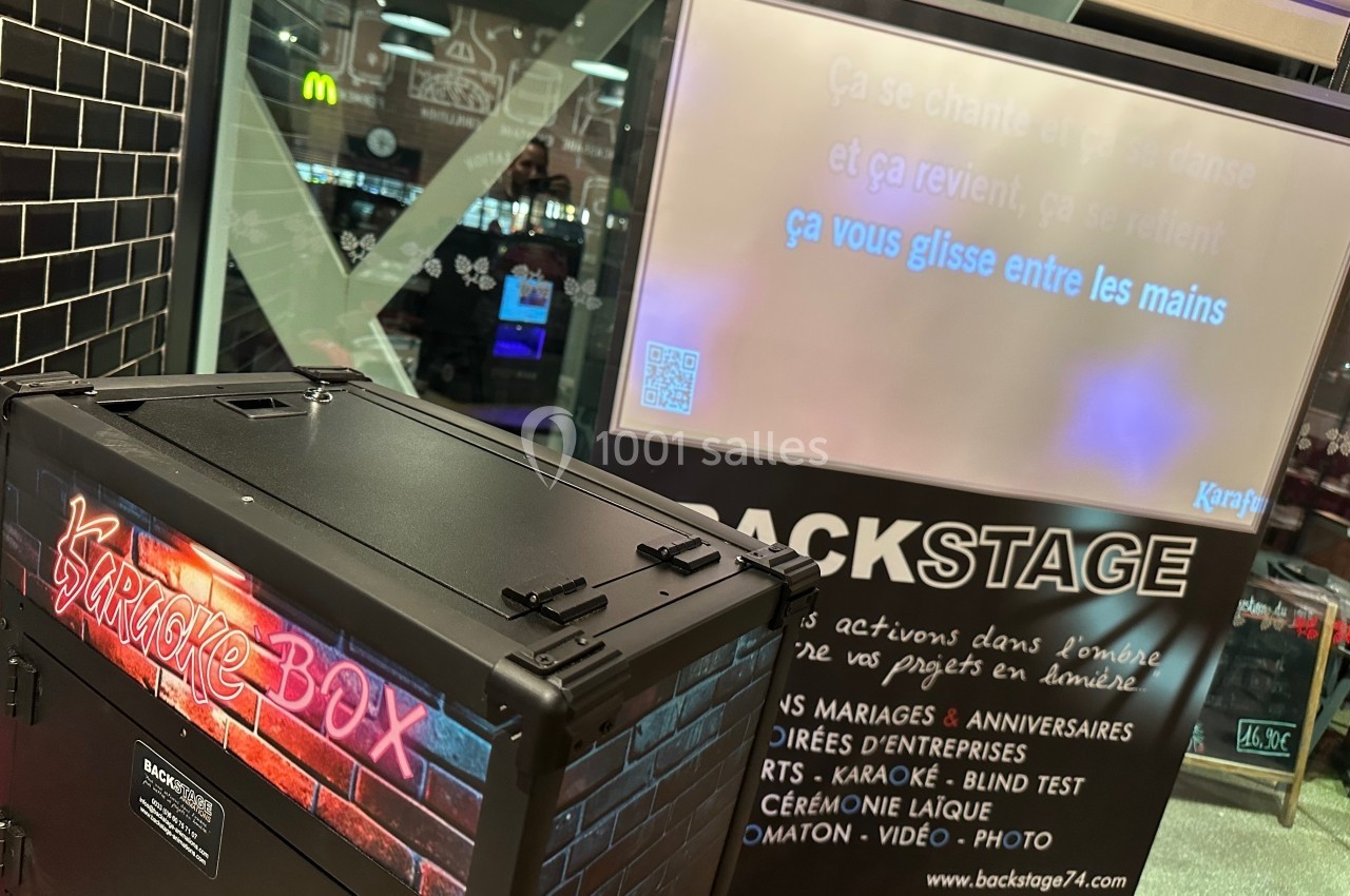 Machine de karaoké avec écran affichant des paroles de chanson dans un espace public éclairé.