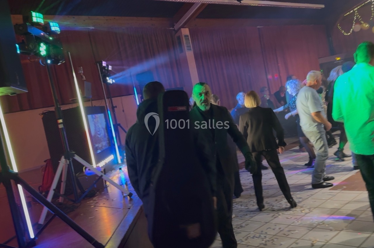 Des personnes dansent et discutent sur une piste éclairée par des projecteurs colorés dans une salle sombre.