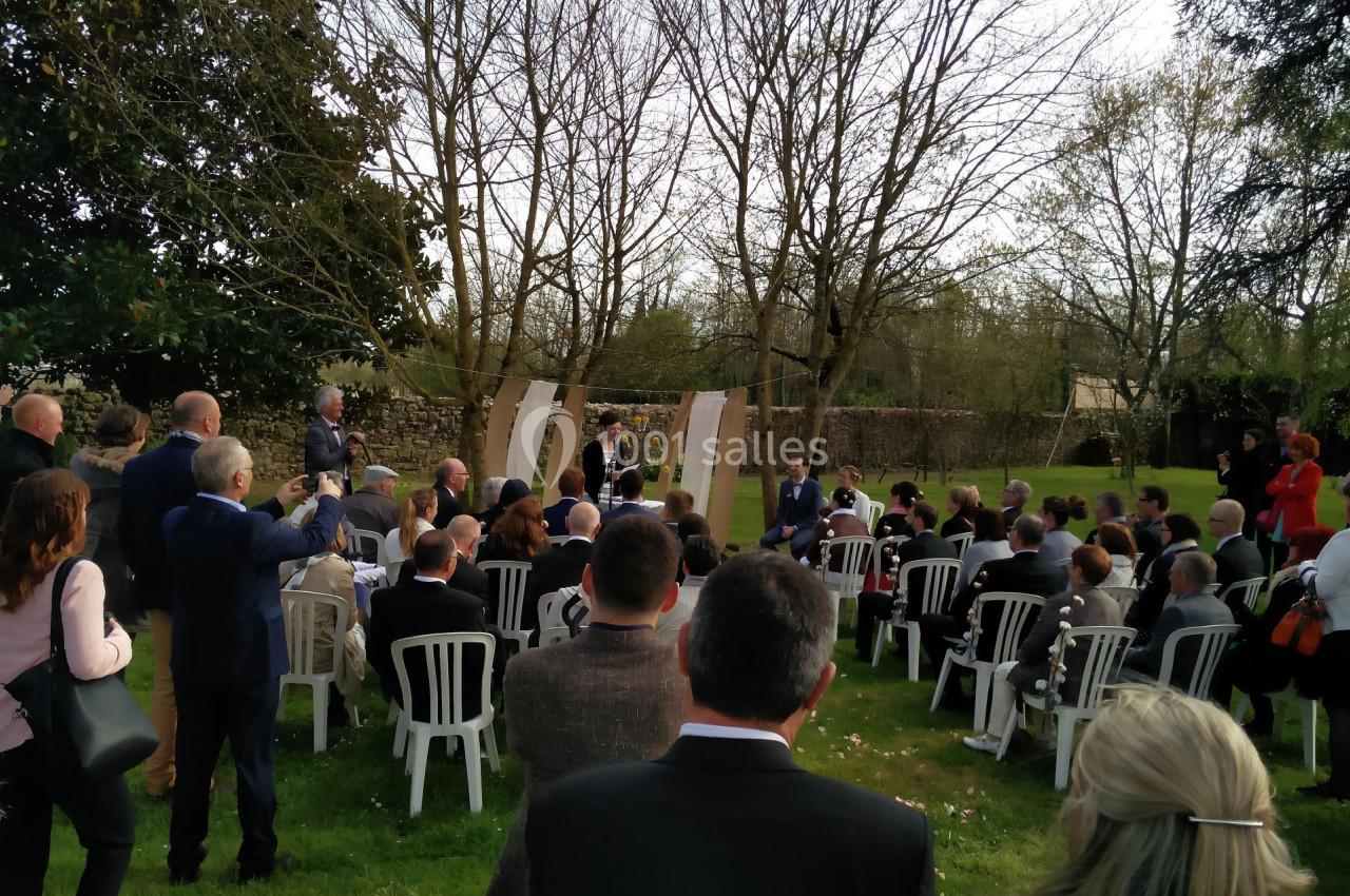 Cérémonie en plein air avec des invités assis sur des chaises blanches, entourés d'arbres et de verdure.