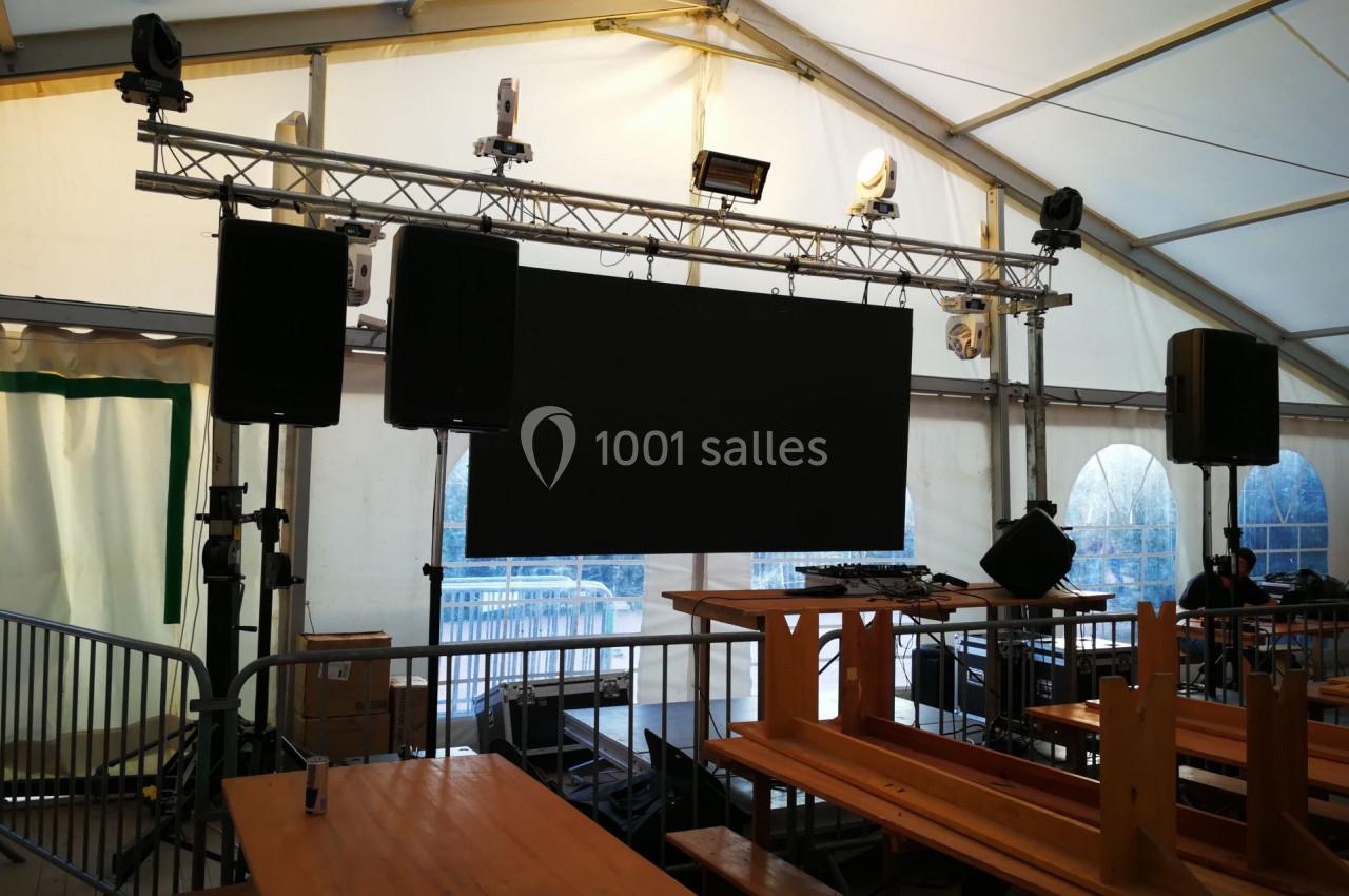 Écran géant suspendu dans une tente équipée de bancs en bois et de matériel audiovisuel.