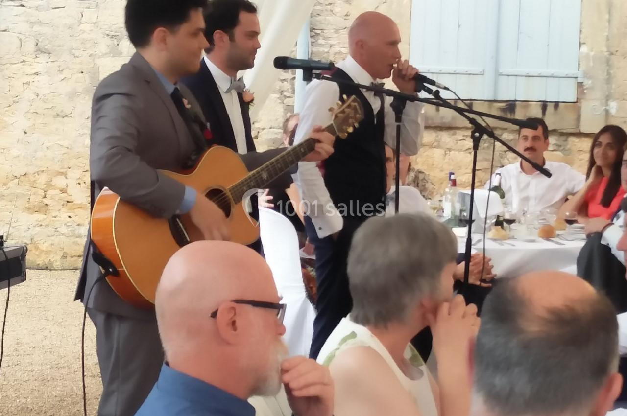 Des musiciens et un chanteur animent un repas en plein air, entourés d'invités assis à des tables.
