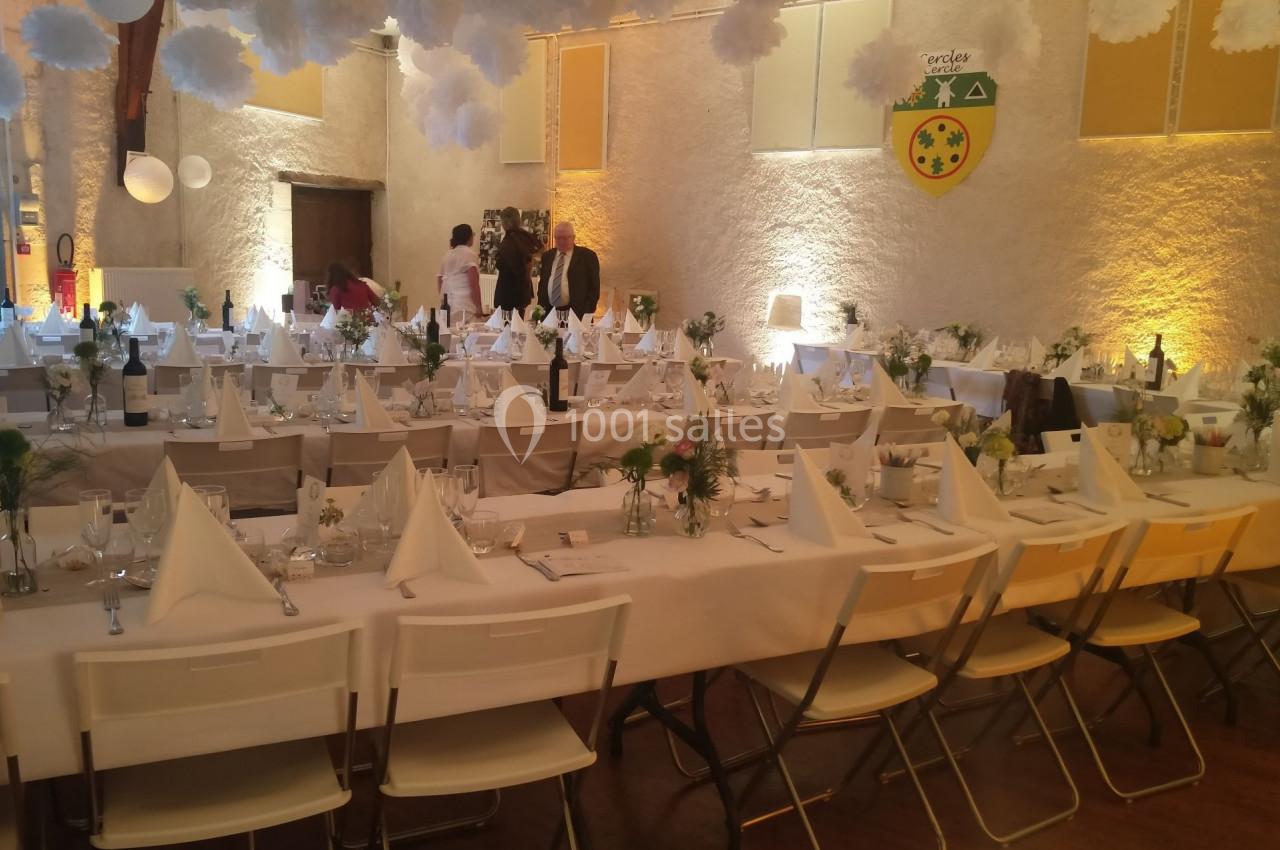 Salle de réception décorée avec des tables dressées, nappes blanches, serviettes pliées et arrangements floraux.