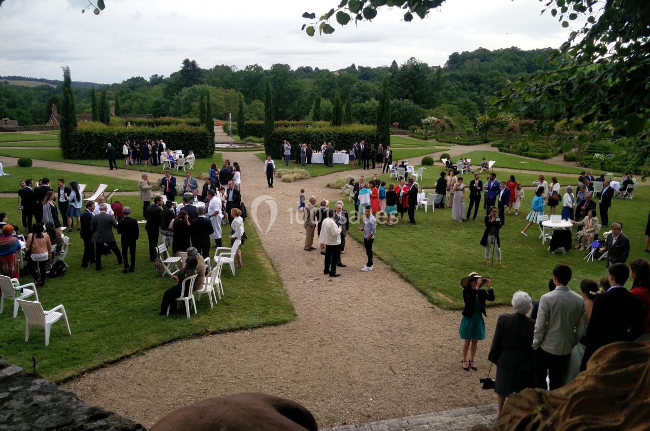 Groupe de personnes rassemblées dans un jardin pour un événement en plein air, entouré de pelouses et d'arbres.